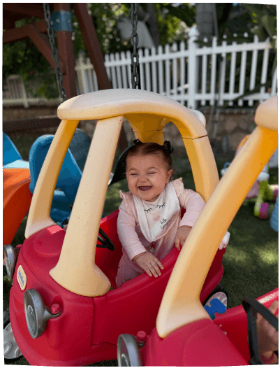 Happy toddler girl in toy car outdoors at Mama Bear Daycare, daycare in Lake Forest.