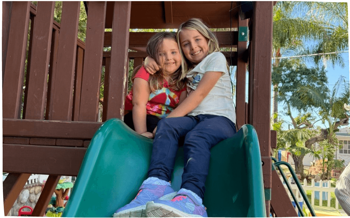 Two girls sitting together on a playground slide, smiling, enjoying the daycare program at Mama Bear Daycare.