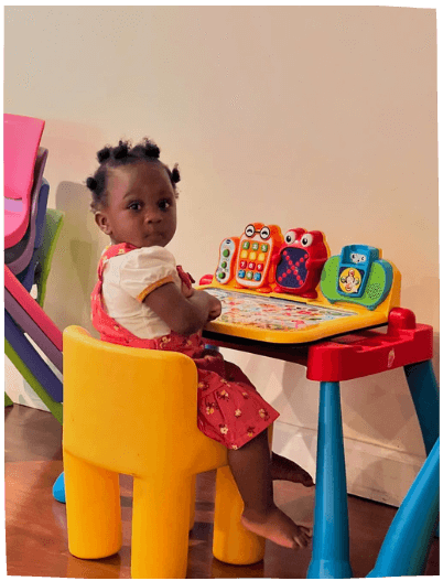 Toddler girl playing with an educational toy at a colorful table indoors, part of Mama Bear Daycare's engaging daycare program.