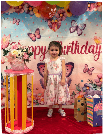 Young girl standing in front of a butterfly-themed birthday backdrop, celebrating at Mama Bear Daycare's daycare program event.